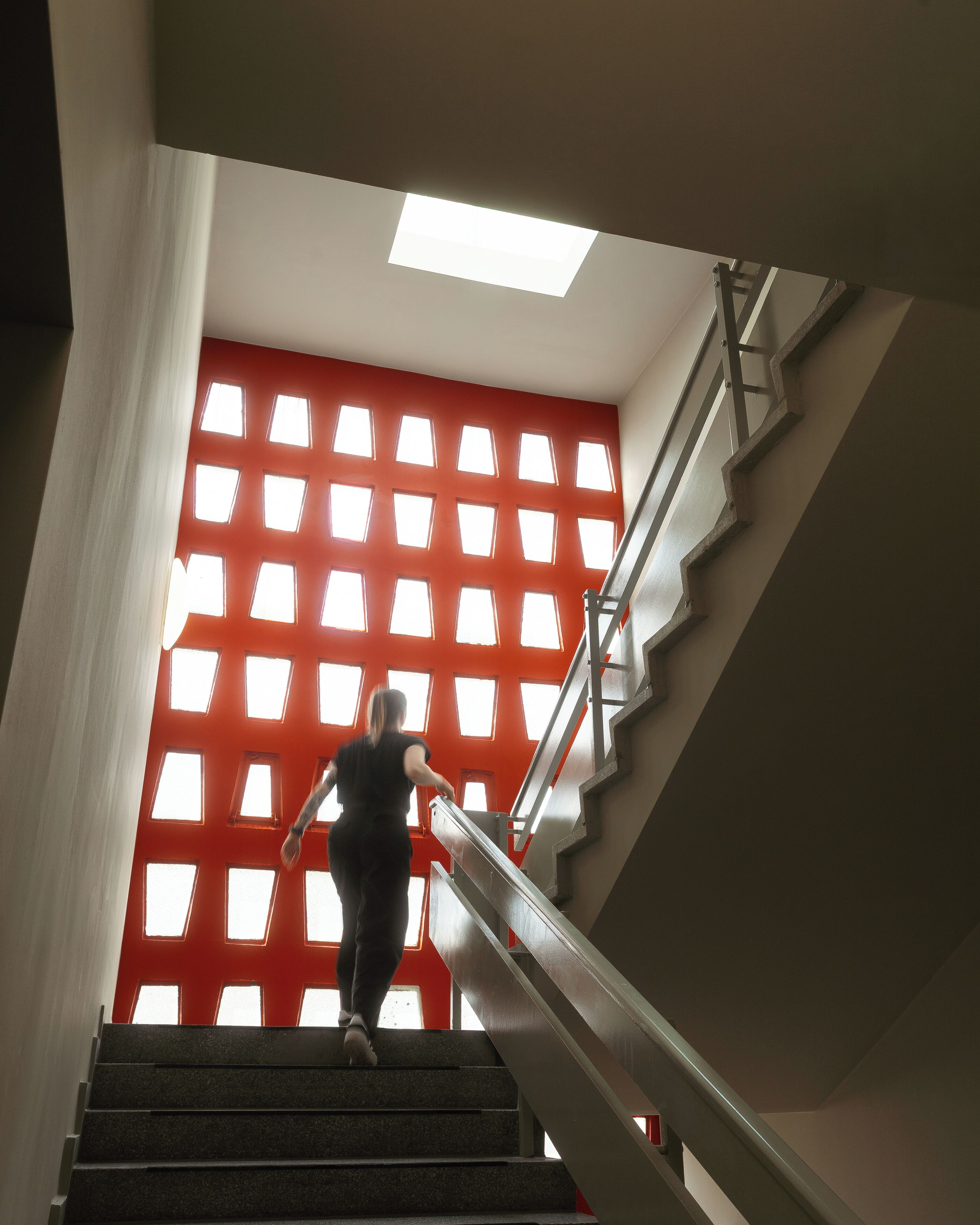 Eine Person steigt eine Treppe hinab, an einer roten Wand mit Oberlicht.