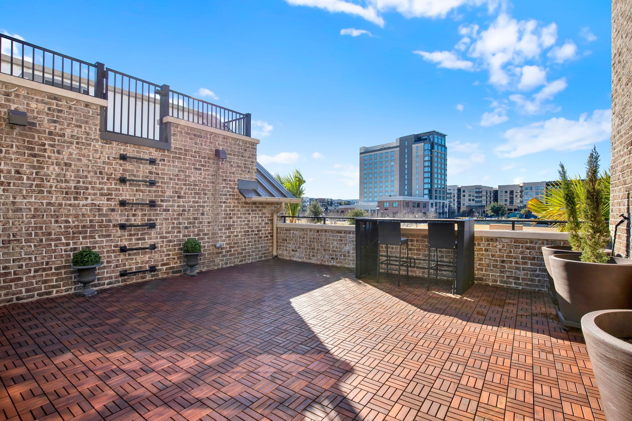A rooftop patio with a brick floor, metal railing, and potted plants.
