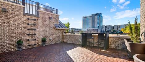 A rooftop patio with a brick floor, metal railing, and potted plants.
