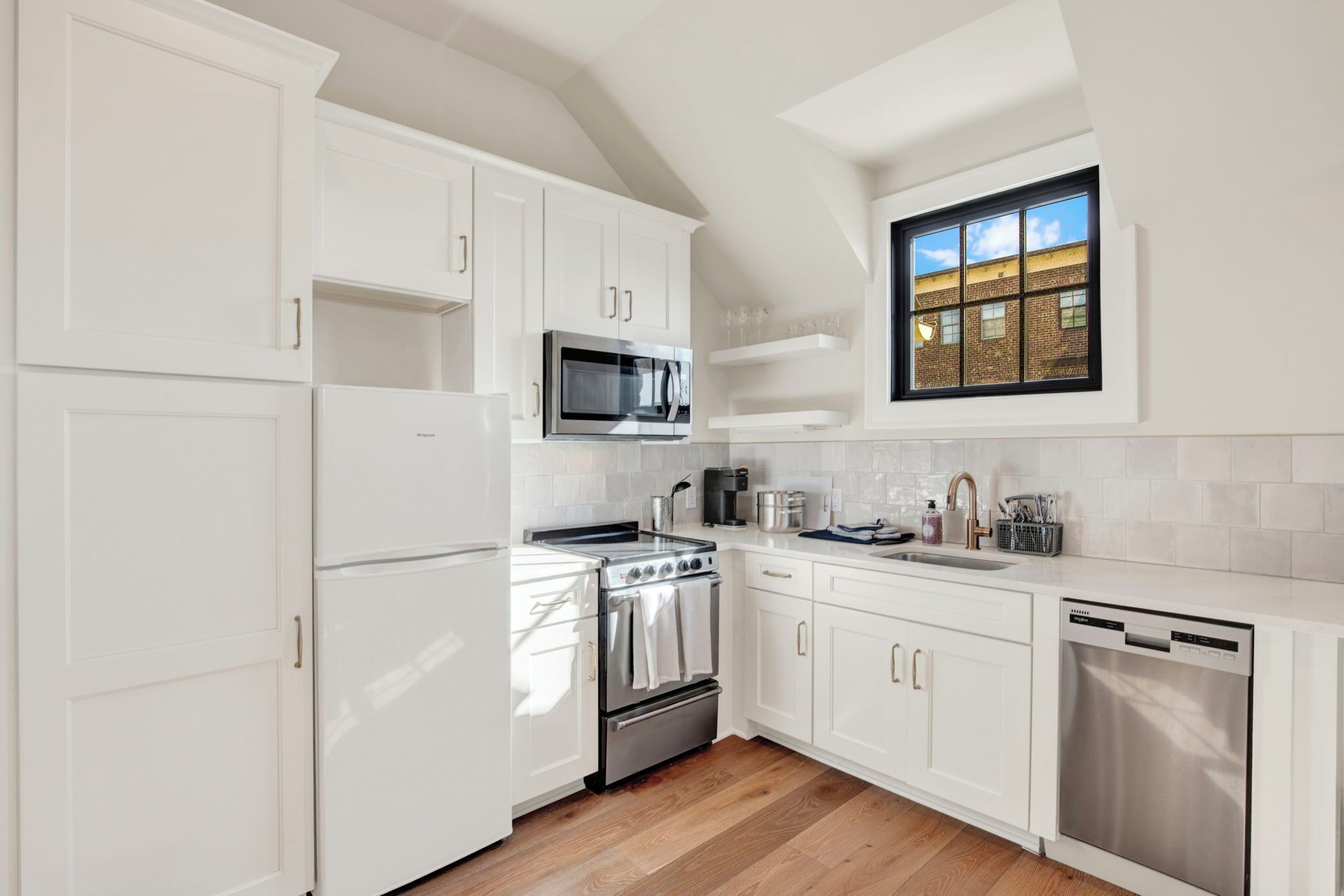 Una cucina moderna con mobili bianchi, elettrodomestici in acciaio inossidabile e una finestra vista su un edificio.
