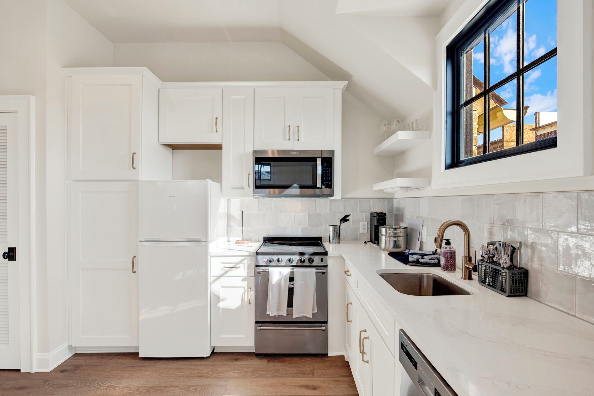 A modern kitchen with white cabinetry, a stainless steel stove, a microwave, and a window with a view.