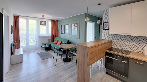 A modern kitchen with a built-in oven, a dining area with a round table and chairs, and a living area with a sofa and a coffee table. - RentPlanet - Apartament Zielińskiego (Wrocław)