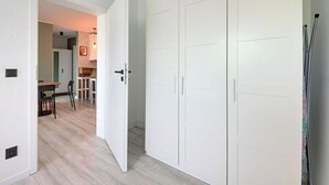 A room with a white wardrobe, a dining area with a table and chairs, and a kitchen area with a patterned wall. - RentPlanet - Apartament Zielińskiego (Wrocław)