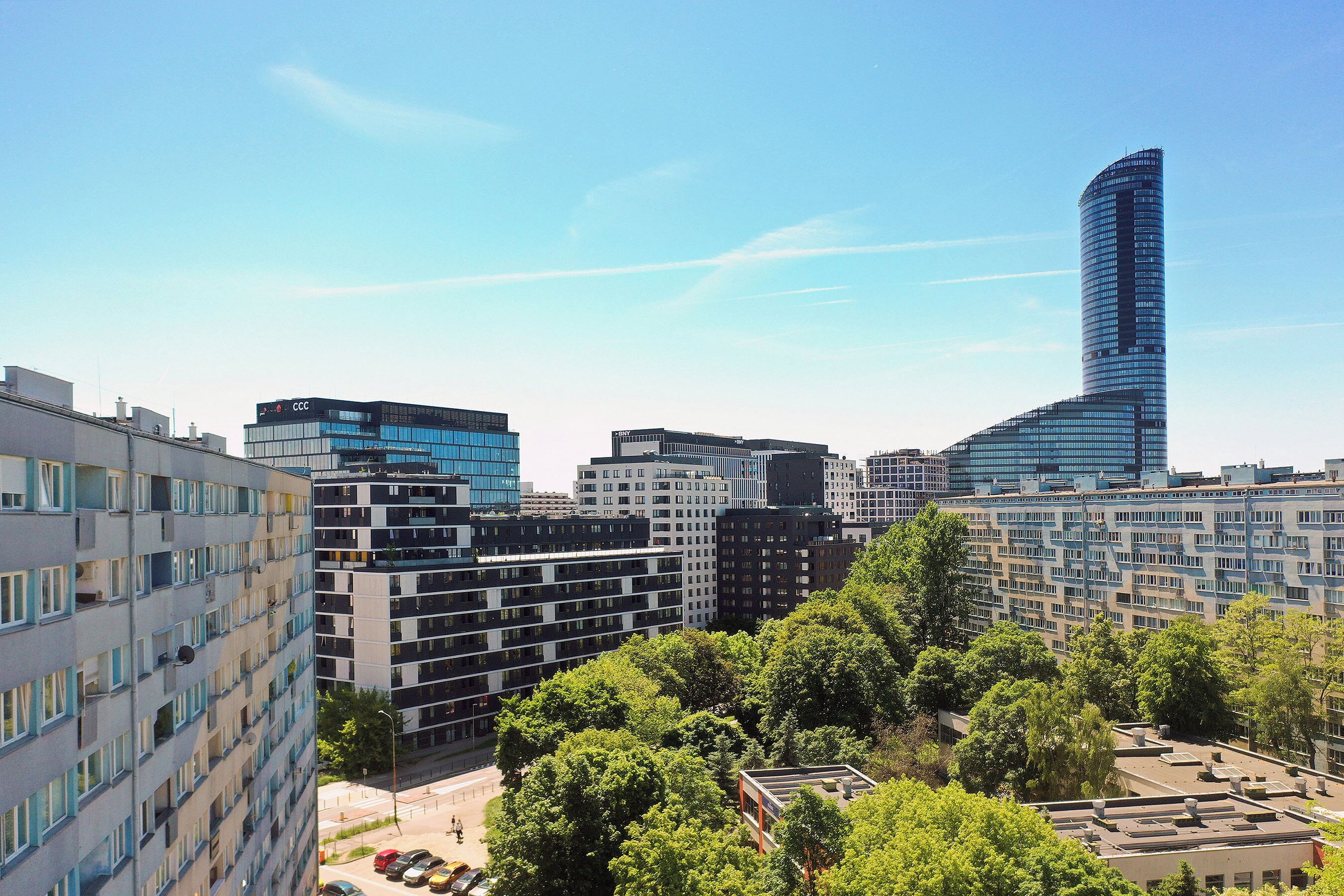 A cityscape with modern buildings, a prominent curved skyscraper, and a park area with trees.