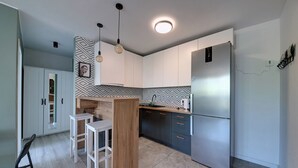 A modern kitchen with a built-in island, white bar stools, a stainless steel refrigerator, and a patterned backsplash. - RentPlanet - Apartament Zielińskiego (Wrocław)