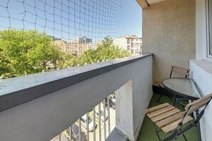 Un balcon donnant sur des immeubles, une table et deux chaises.