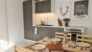 A modern kitchen with grey cabinets, a white countertop, and a dining table set with plates and a book. - Apartment 'Hirschkönig' with Mountain View (Bad Lauterberg im Harz)