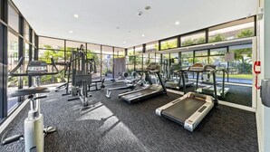 Un gimnasio con diverso equipo de ejercicio, amplias ventanas y suelo alfombrado.