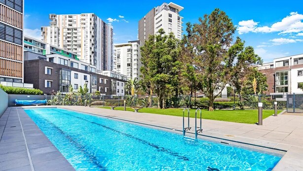 Piscina con agua cristalina azul, rodeada de edificios modernos y árboles.