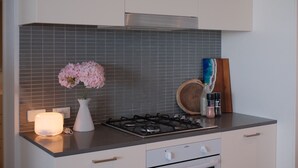 Una cocina con estufa a gas, gabinetes blancos, salpicadero de azulejos, un florero con flores y una tabla de cortar de madera.