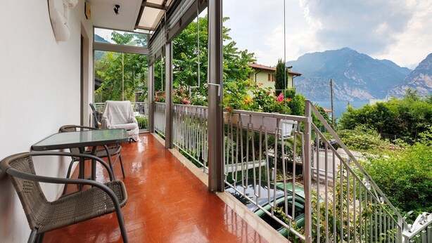 A balcony with a table and chairs, a view of mountains, and a car parked outside. - Apartment 'Bilocale Ulrica' with Private Terrace and Wi-Fi (Nago–Torbole)