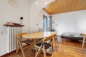 Een kamer met een ronde tafel, stoelen, een bed, een radiator, een klok en een raam.