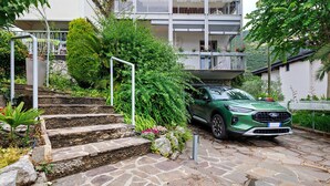 A green SUV parked on a stone staircase leading to a building with balconies and a garden. - Apartment 'Bilocale Ulrica' with Private Terrace and Wi-Fi (Nago–Torbole)
