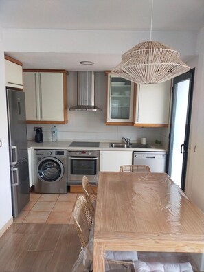 A compact kitchen with a washing machine, oven, and a dining area with a table and chairs.