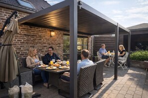 A covered outdoor dining area with brick walls, wicker furniture, and a table set for a meal. - “Exclusive Chateau Estate, for 14 Guests with Pool Near Tongeren” (Tongeren-Borgloon)