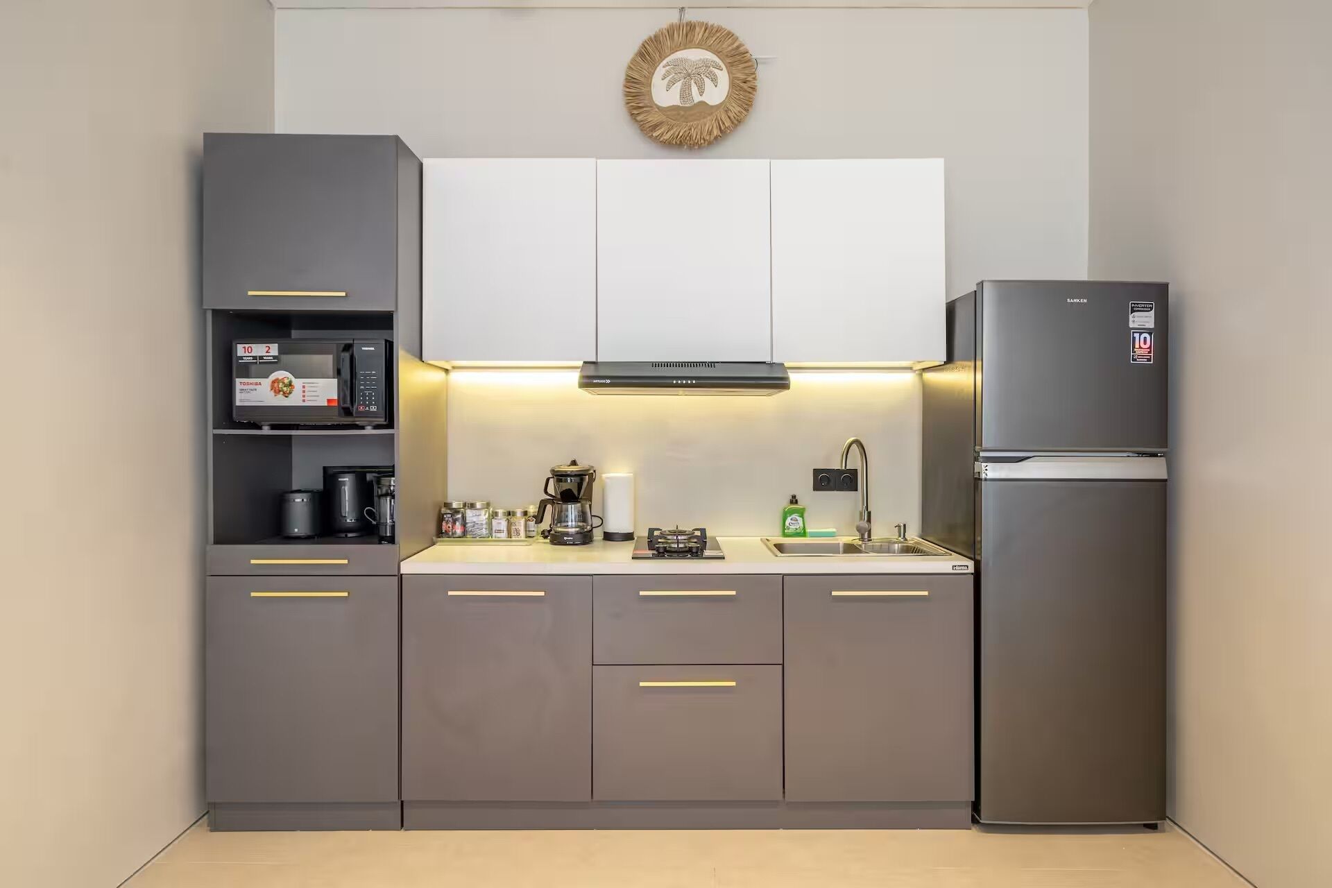 Una cocina moderna con gabinetes grises, un refrigerador de acero inoxidable, un microondas y una cafetera.