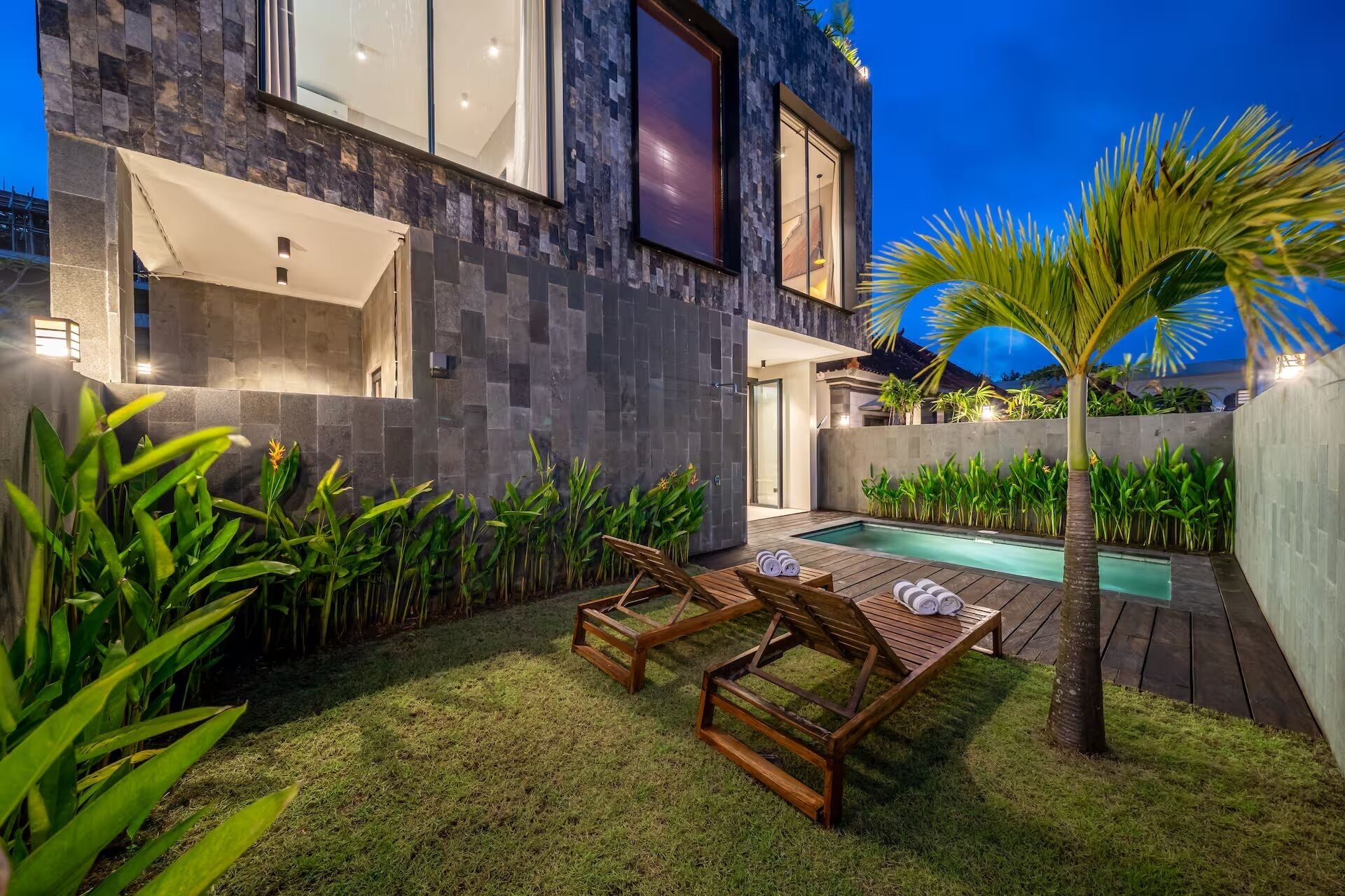 A modern house with a swimming pool, outdoor furniture, and tropical plants.