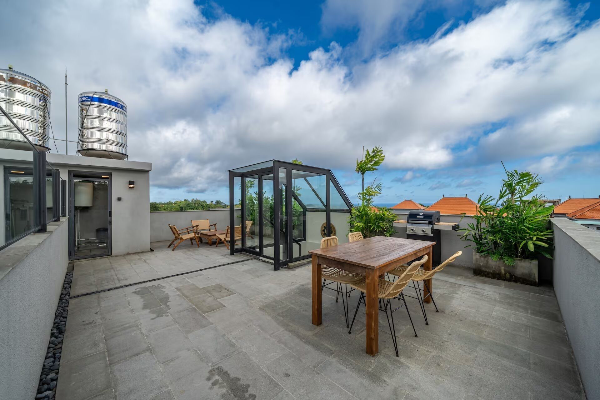 Terraza en la azotea con mesa y sillas de madera, cerramiento de vidrio y depósitos de agua.