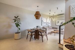 A modern dining area with a round table, chairs, a hanging light fixture, and a potted plant.
