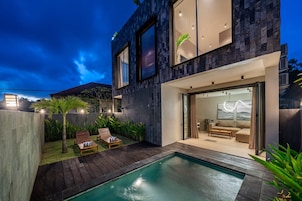 A modern house with a swimming pool, outdoor seating, and a large glass door leading to a living area.