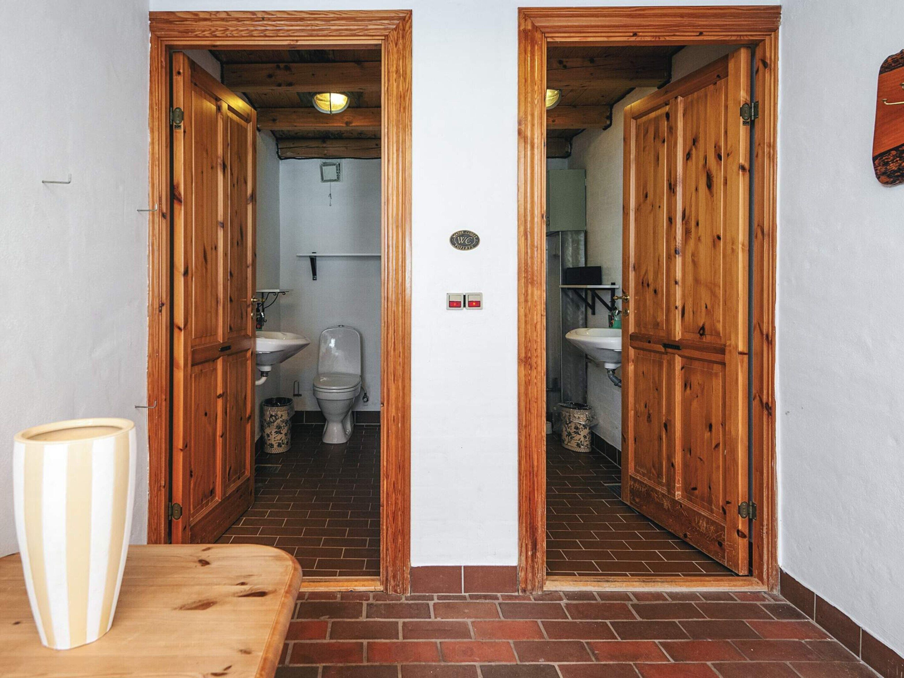 A bathroom with wooden doors, a toilet, a sink, and a trash bin.