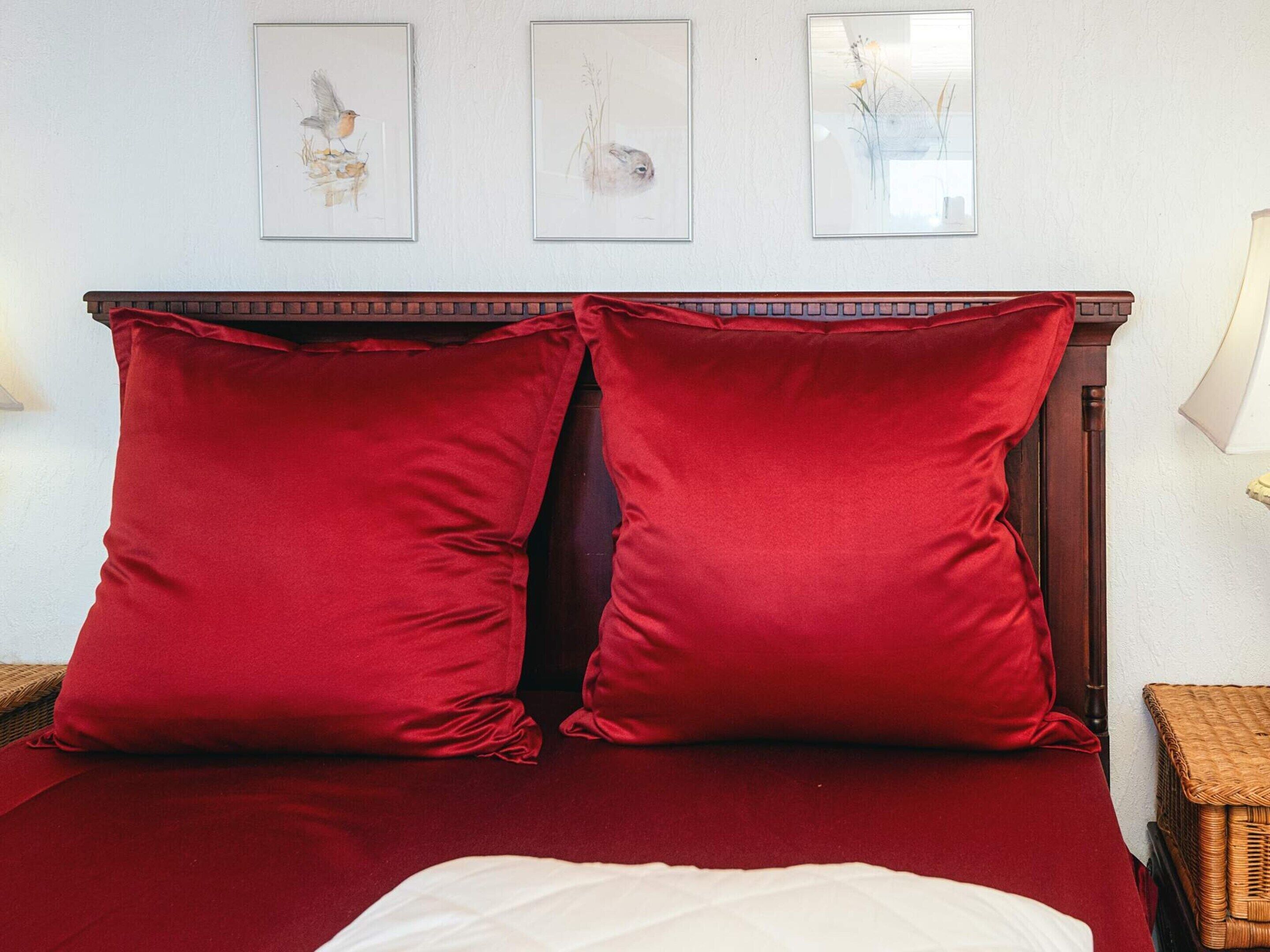 A bed with red bedding, two red pillows, and three framed artworks on the wall.
