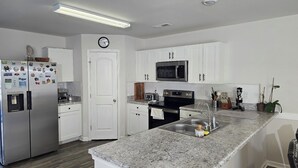 Una cocina moderna con armarios blancos, electrodomésticos de acero inoxidable, encimera de granito y microondas integrado.