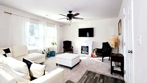 Una sala de estar con sofá, reposapiés, sillas, chimenea, televisor y ventilador de techo.