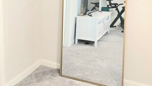 Una habitación con un espejo grande, un aparador blanco y un cuadro en la pared.