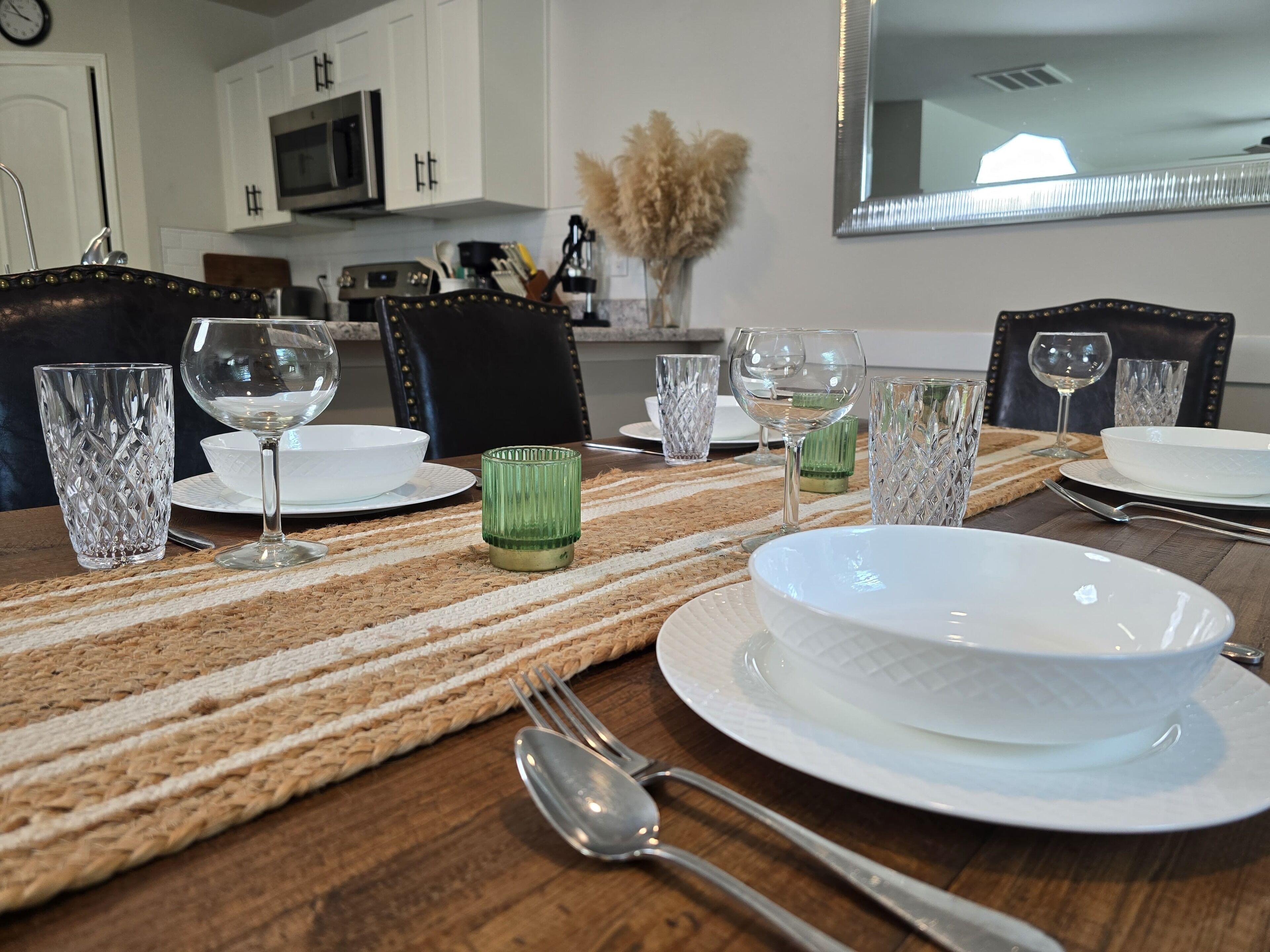 A dining table set with white plates, clear glasses, and cutlery, with a woven placemat.