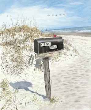Ein Briefkasten mit dem Schriftzug 'Kindred Spirit' an einem sandigen Strand mit Gras und Blick auf den Ozean.