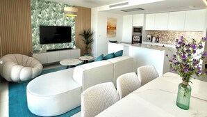 A modern living room with a sofa, TV, and a dining area with a table and chairs. - Luxury Penthouse with the view (Estepona)