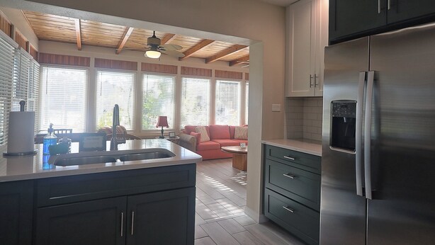 Eine Küche mit einem Edelstahl-Kühlschrank, Holzbalkendecke und Blick in einen Wohnbereich mit einer Couch.