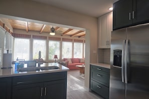 Eine Küche mit einem Edelstahl-Kühlschrank, Holzbalkendecke und Blick in einen Wohnbereich mit einer Couch.