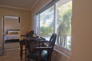 Ein Zimmer mit einem Bett, einem Esstisch mit Stühlen und einem großen Fenster mit Blick auf Palmen.