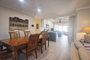 Ein Essbereich mit Holztisch und -stühlen, im Hintergrund eine Küche und ein Wohnzimmer mit einer Couch.