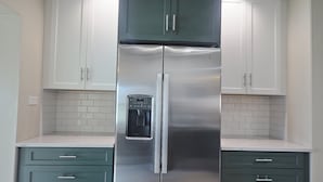 Ein Kühlschrank aus Edelstahl mit Wasserspender, weiße Schränke und Kommoden in Türkis in einer Küche.