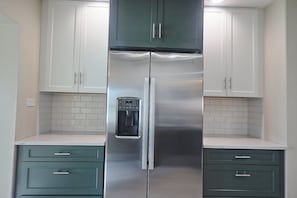 Ein Kühlschrank aus Edelstahl mit Wasserspender, weiße Schränke und Kommoden in Türkis in einer Küche.