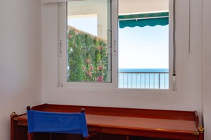 Ein Zimmer mit einer Holzbank, einem Fenster mit Meerblick und einem Balkon mit grüner Markise.