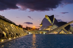 Ein Gebäude direkt am Wasser mit markantem architektonischem Design, das sich durch große, geschwungene weiße Strukturen und eine spiegelnde Wasseroberfläche auszeichnet.