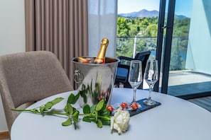 Una mesa con una botella de champán en un balde de metal, dos copas de vino, una rosa y una rama de hojas verdes.