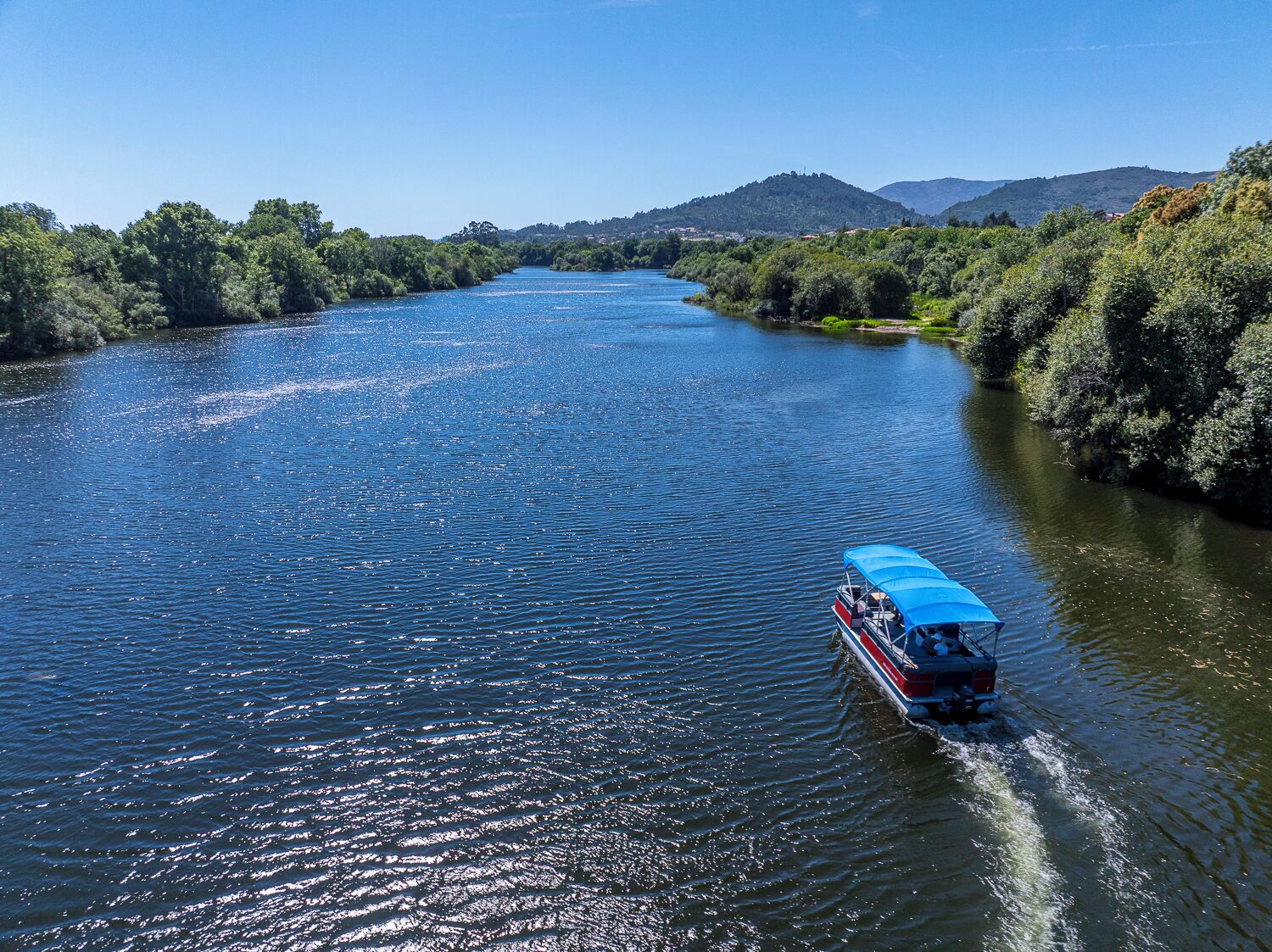 Um rio com um barco deslizando sobre suas águas, cercado por vegetação e colinas.