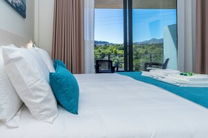 Una habitación de hotel con cama, vistas al exterior y un balcón con sillas.