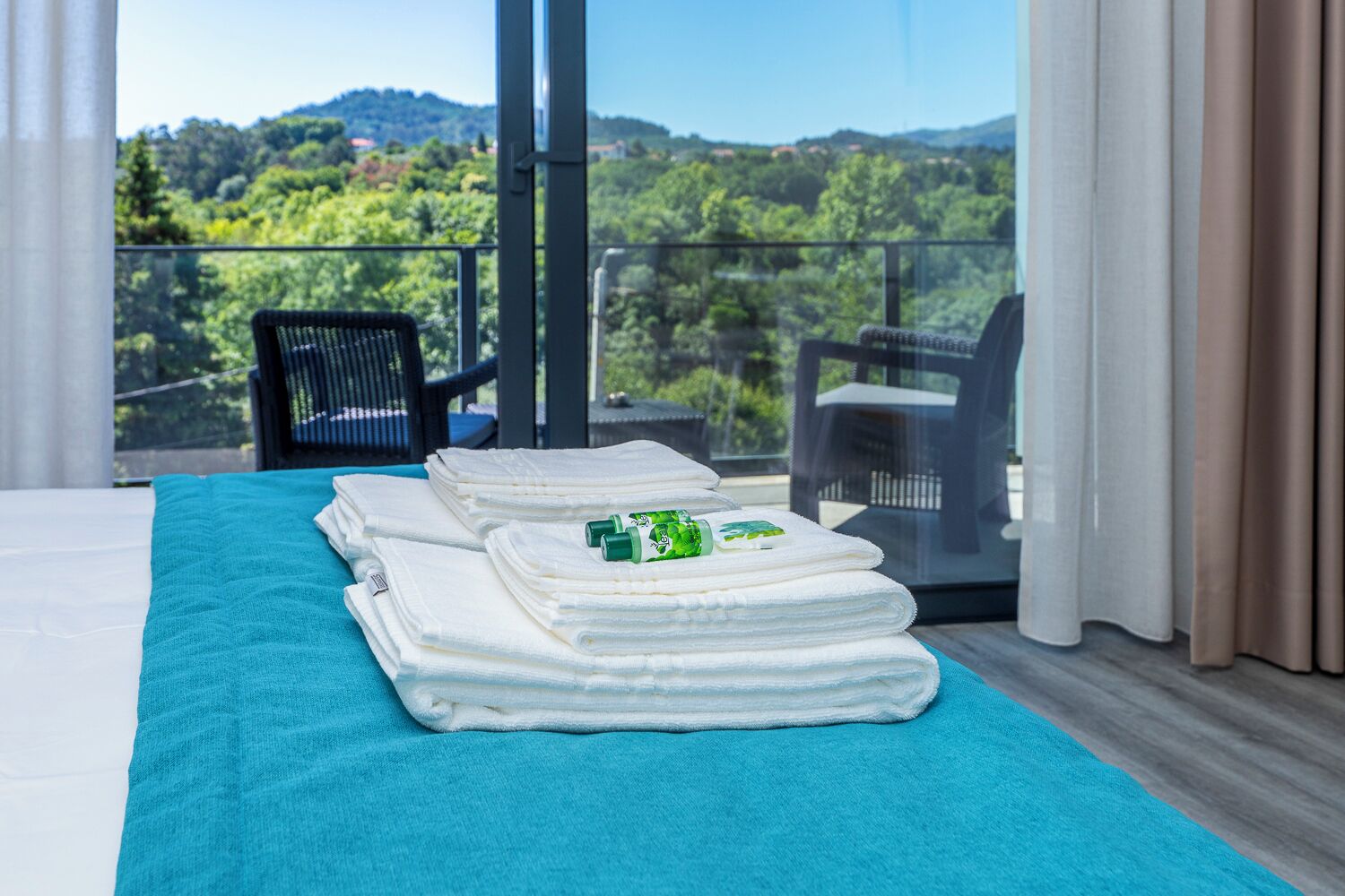 A hotel room with a bed, a balcony with a view of the countryside, and a chair.