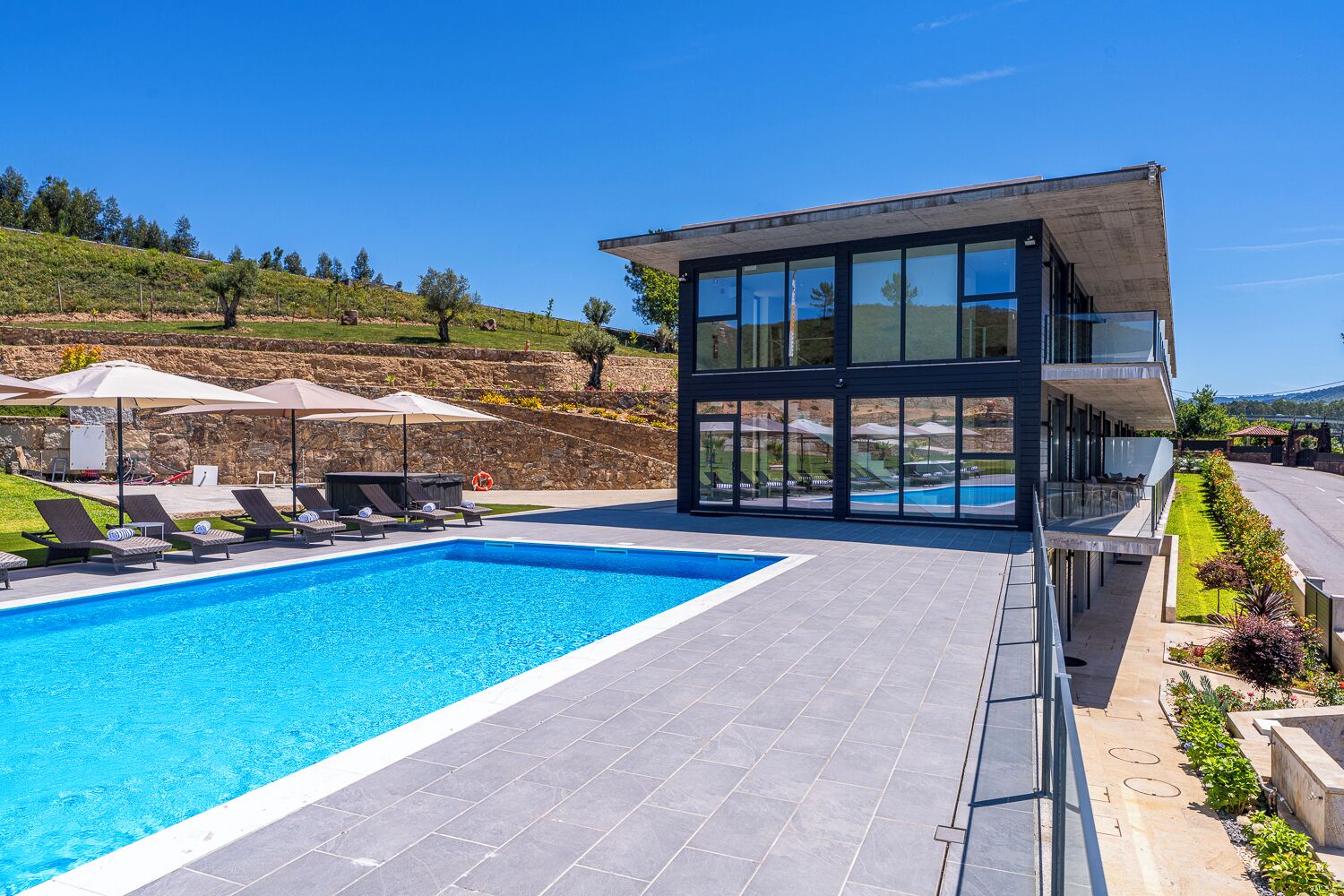 Un edificio moderno con piscina, sillones reclinables y sombrillas.