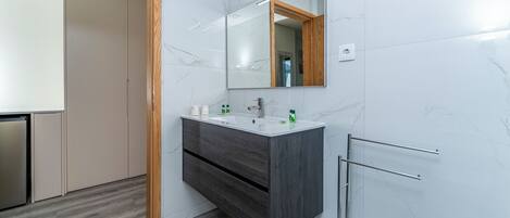 A modern bathroom with a marble wall, a wooden door, a dark wood vanity, and a glass shower enclosure.