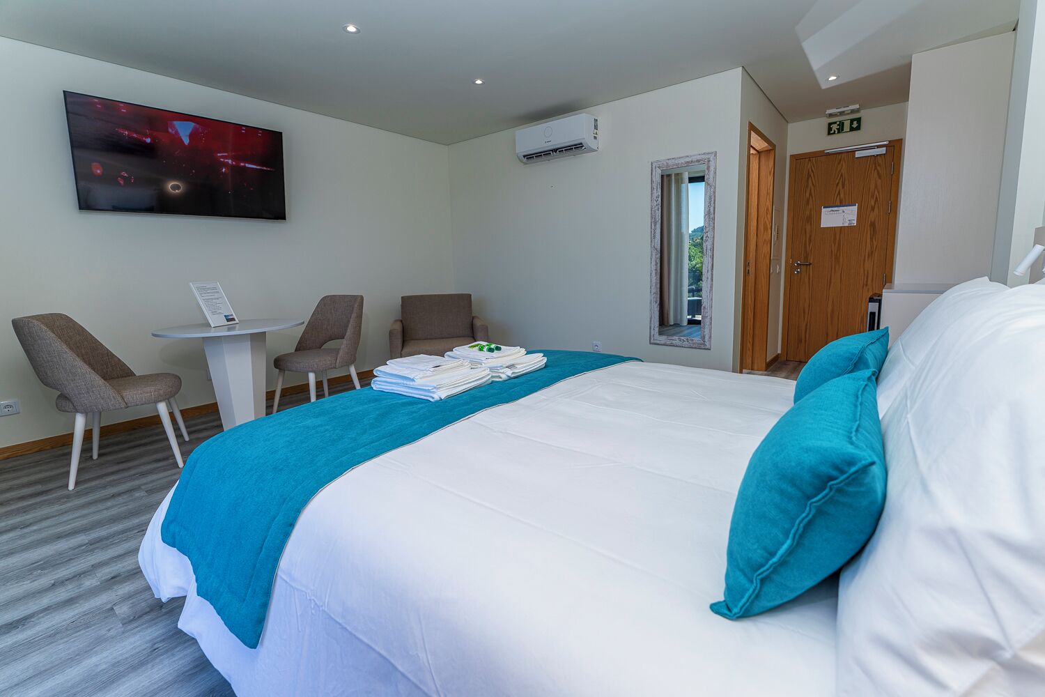 Ein Hotelzimmer mit Bett, Fernseher, Schreibtisch, zwei Stühlen und einer Tür.