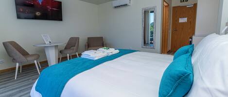Ein Hotelzimmer mit Bett, Fernseher, Schreibtisch, zwei Stühlen und einer Tür.