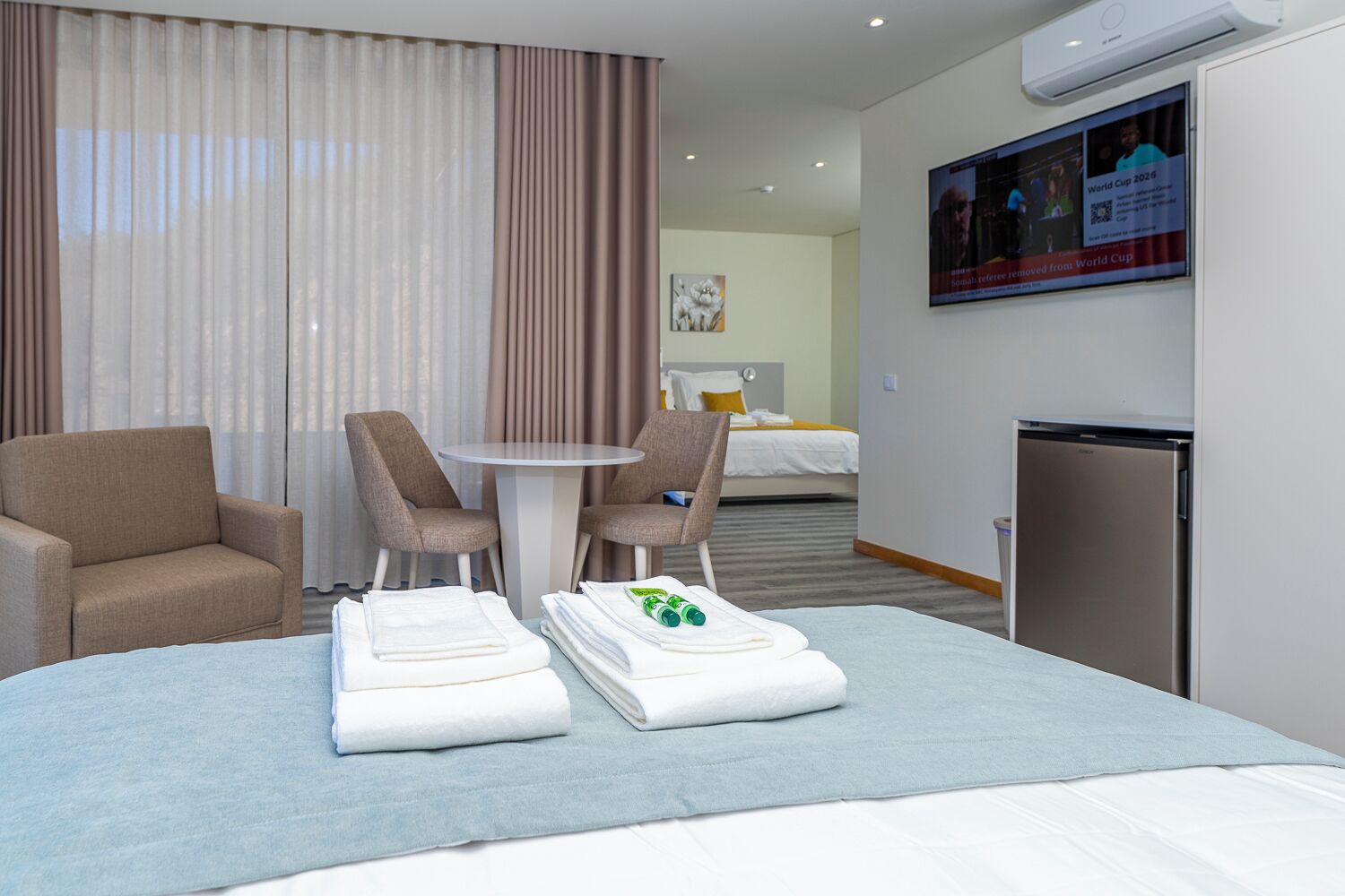Habitación de hotel con cama, dos sillones, una mesita, televisión y minibar.