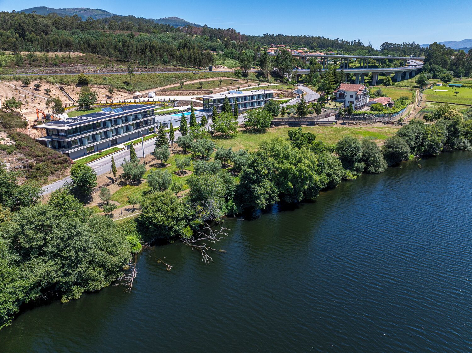 Un ensemble d’immeubles modernes situés au bord d’une rivière, avec un pont en arrière-plan.